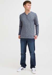 Majica dugih rukava, navy heather boje s Henley ovratnikom, tri dugmeta i kontrastnim šavovima. Uparena s plavim trapericama i bijelim tenisicama.