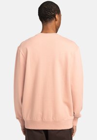 Light pink crewneck sweatshirt with a relaxed fit, ribbed cuffs and hem, and smooth texture. Features a small logo tag on the side.