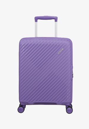 Valigia rigida viola con scanalature diagonali, manico telescopico, quattro ruote girevoli e logo American Tourister sulla parte anteriore.