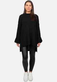 Maglione nero oversize a coste con maniche a campana, abbinato a leggings neri e sneakers bianche. Il maglione presenta un design con orlo asimmetrico.