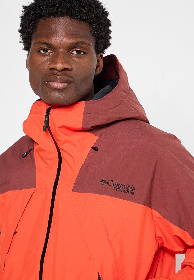 Rote und braune wasserfeste Jacke mit Kapuze, ausgestattet mit Reißverschlüssen und einem Logo auf der Brust. Der Stoff wirkt glatt und langlebig.