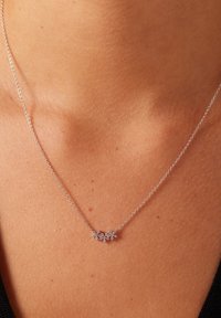 Zilveren ketting met een bloemenvormige hanger, versierd met kleine stenen in een clusterontwerp. Soepele textuur, delicate uitstraling.