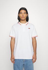 Biała koszulka polo z kontrastowymi kołnierzykiem i mankietami w paski w kolorze czerwonym, żółtym i pomarańczowym. Posiada małe haftowane logo na lewej piersi.