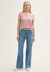 Blouse à manches courtes rouge et blanche à motifs, associée à un jean bleu clair évasé et une ceinture beige clair, le tout complété par des baskets blanches.