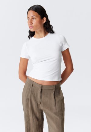 White cropped t-shirt with short sleeves, paired with brown, loose-fitting trousers featuring a textured, subtle pattern.