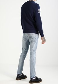 Námořnický svetr s kulatým výstřihem a bílým číslem na rukávu, kombinovaný se světle modrými džíny a černými botami s mírným podpatkem.