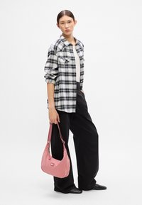 Camisa de franela a cuadros en blanco y negro sobre una blusa beige, pantalones sueltos negros y un bolso de hombro rosa con un parche de logo.