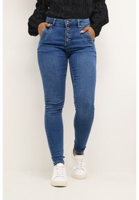 Jeans skinny de denim azul con una cintura alta, cierre de cinco botones y bolsillos frontales, que presentan una textura suave y una silueta ajustada.