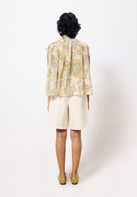 Bloemenpatroon, kortemouwen top in pastelkleuren, gecombineerd met off-white shorts. De top heeft een losse pasvorm en een strikdetail op de rug.