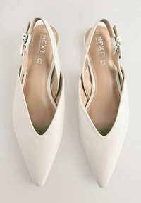 Tassuistuimetsä slingback-kengät pehmeästä valkoisesta nahasta. Varustettu kapealla nilkkahihnalla, jossa on hopeinen koriste, ja pehmustetulla sisäpohjalla mukavuutta varten.