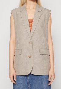 Beige ärmellose Blazer aus strukturiertem Stoff, mit zwei Fronttaschen und einem Reverskragen. Verfügt über zwei Knöpfe und eine lockere Passform.