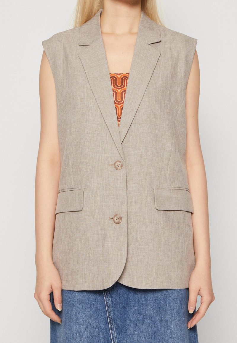 Beige ärmellose Blazer aus strukturiertem Stoff, mit zwei Fronttaschen und einem Reverskragen. Verfügt über zwei Knöpfe und eine lockere Passform.