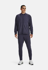 Chándal deportivo color azul marino hecho de un tejido suave y ligero; chaqueta con capucha y cremallera, con bolsillos, combinada con pantalones ajustados y zapatillas blancas.