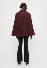 Burgundy kappa med krage, med en flödande design. Parat med svarta utsvängda byxor och klackskor. Slät textur.