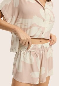 Piżama z krótkim rękawem, zapinana na guziki, w jasnoróżowym kolorze, z dużymi białymi abstrakcyjnymi wzorami; elastyczny pas w szortach. Miękka, lekka tkanina.