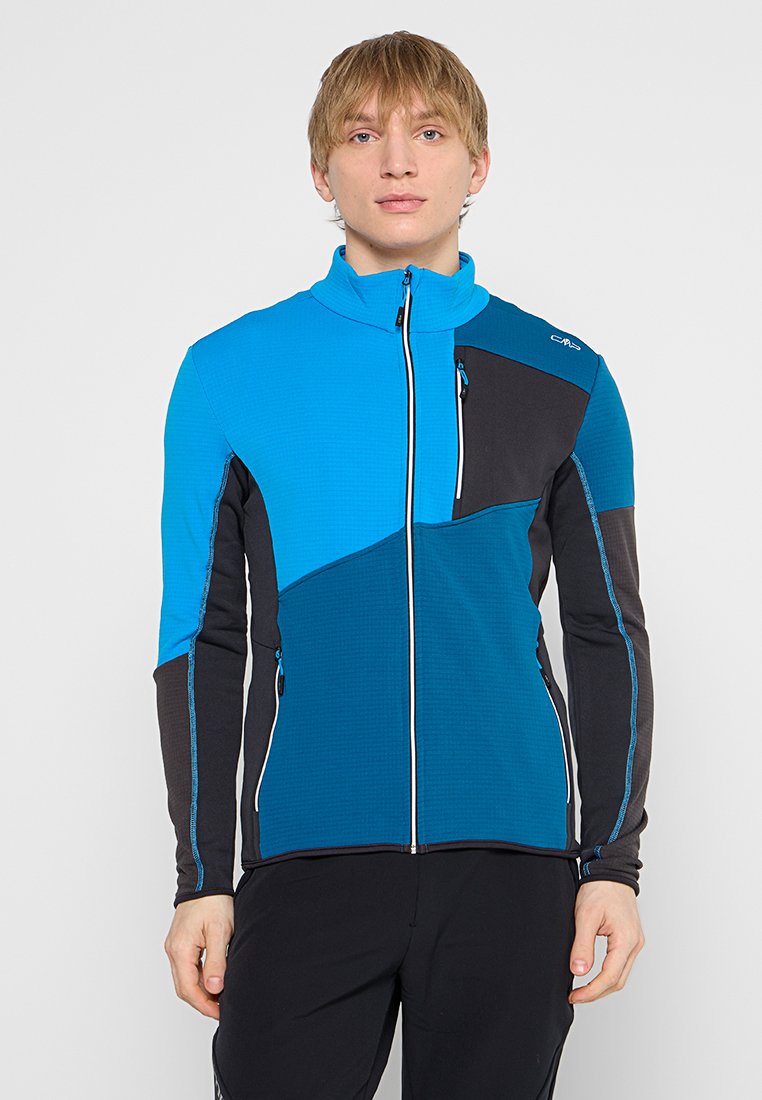 Chaqueta azul y negra con cremallera, cuello alto, tela texturizada y bloques de color contrastantes. Presenta un bolsillo con cremallera en el pecho.