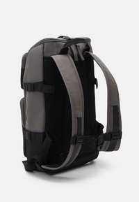 Grau fabric Rucksack mit verstellbaren gepolsterten Trägern, Netzrücken, seitlichen Schnallen und einem Reißverschluss oben. Glatte Textur mit verstärkten Nähten.
