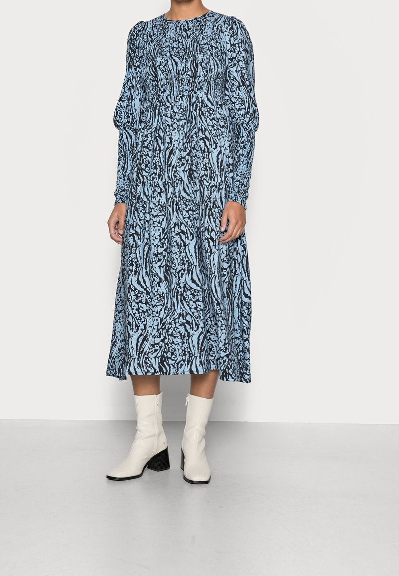 Sininen ja musta kuviollinen pitkähihainen mekko, jossa on rypytetty vyötärö ja valuva hame, yhdistetty valkoisiin nilkkabootseihin ja kerrostettuihin korkoihin.