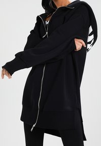 Black zip-up hoodie made of soft fabric, featuring a relaxed fit, oversized design, long sleeves, and a side zipper detail.