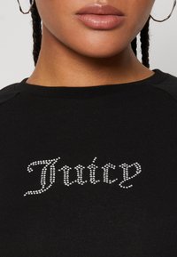 Black sweatshirt featuring "Juicy" in rhinestones, with a smooth texture and fitted design, round neckline and raglan sleeves.