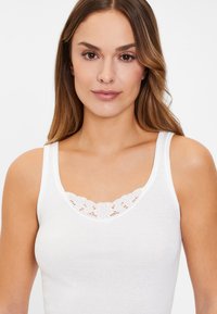 White tank top made from soft cotton with a lace trim at the neckline. Features wide straps and a fitted silhouette.