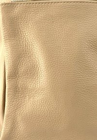 Sac à main en cuir beige avec une finition texturée, featuring une fermeture éclair lisse et des plis subtils, mettant en valeur un matériau souple et flexible.