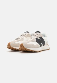 Light beige and black athletic shoes with a suede and mesh design, featuring a textured sole and contrasting rubber outsole.