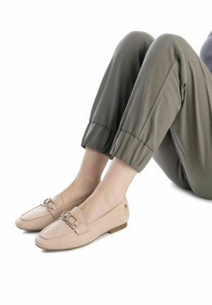 Mocasines de ante beige con un diseño de punta cuadrada y detalle decorativo de hebilla. Tacón bajo apilado y suela texturizada. Combinados con pantalones verdes olivo con puños.