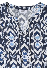 Blusa con estampado azul y blanco con escote en V, cordones trenzados que terminan en cuentas y borlas, y una etiqueta "CECIL" en el escote.