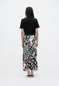 Čierne tričko v kombinácii s dlhou sukňou s viacfarebnými vzormi zvierat a hviezd; hladká látka a priliehavý pás.