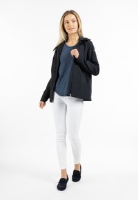 Giacca leggera nera con una camicia a righe blu sotto, abbinata a jeans skinny bianchi e mocassini neri. Texture liscia, design casual.