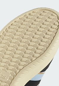 Beige Schuhsohle mit strukturierten kreisförmigen Mustern und teilweise sichtbarem schwarzem und blauem Obermaterial.