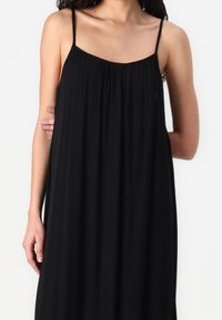 Černé bezramínkové šaty s volným designem, strukturovanou tkaninou a řaseným výstřihem. Obsahují tenké ramínka a volný střih.
