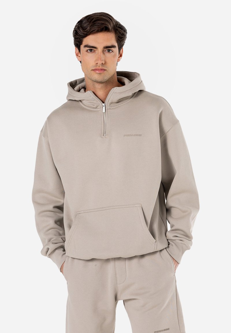 Beige hoodie med lynlås, som har en frontlomme, hætte med snore og en blød, glat tekstur. Minimalistisk branding synlig på brystet.