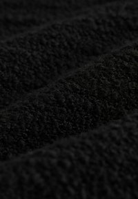 Czarny, teksturowany materiał o miękkiej, puszystej powierzchni. Materiał ma grubą, pluszową strukturę z widocznymi włóknami, tworzącymi bogatą głębię.