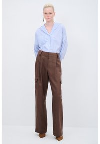 Blau-weiß gestreifte Bluse mit Kragen, kombiniert mit braunen Cargo-Hosen mit hohen Taillen und Taschen. Das Model trägt braune High Heels.