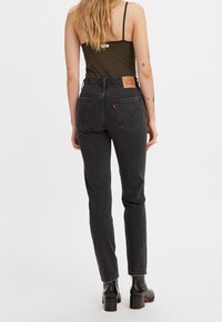 Jeans de denim negro con corte de pierna recta, cintura alta y bolsillos traseros. Presentan una etiqueta de cuero en la pretina y un dobladillo deshilachado.