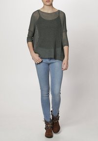 Suéter gris de punto suelto con escote amplio y mangas tres cuartos, combinado con jeans skinny de color azul claro y botas cortas marrones.