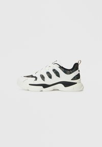 Weiße und schwarze Sneaker mit Camouflage-Stoffeinsätzen, dicker weißer Sohle, Schnürverschluss vorne und Zuglasche an der Ferse.