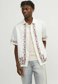 Hvid kortærmet skjorte med brun blomsterbroderi på forsiden og ærmerne. Har en knaplukning og letvægtsstof.