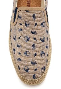 Zapato beige de tipo slip-on con una parte superior de tejido texturizado que presenta un patrón de manchas azul oscuro. Suela de fibra natural y acentos elásticos a los lados.