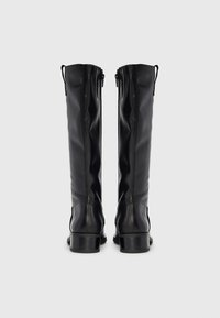 Μαύρα μποτάκια μέχρι το γόνατο με λείο δερμάτινο φινίρισμα, εξοπλισμένα με φερμουάρ και γερά, χοντρά τακούνια, σχεδιασμένα με λιτές λεπτομέρειες.