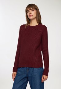 Bordowy sweter z dzianiny o teksturowanym wzorze, z okrągłym dekoltem i ściągaczami, w połączeniu z niebieskimi dżinsami.