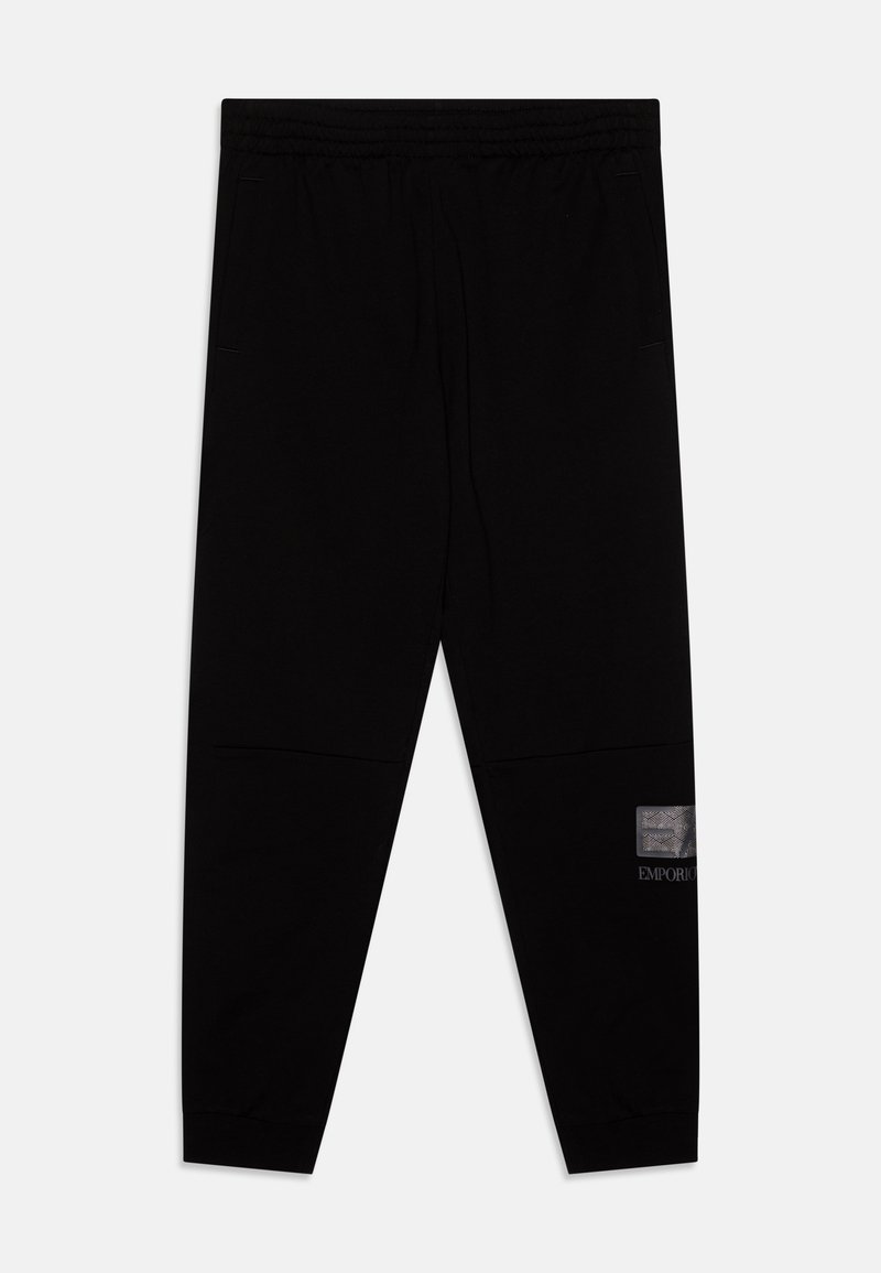 Pantalon de jogging noir avec une taille élastique, poches latérales, texture lisse et un écusson en métal argenté sur une jambe.