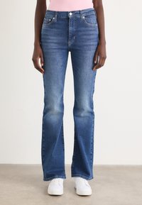 Bredde blå jeans laget av denim med middelsvask. Har frontlommer og knappefeste. Kombinert med hvite joggesko.
