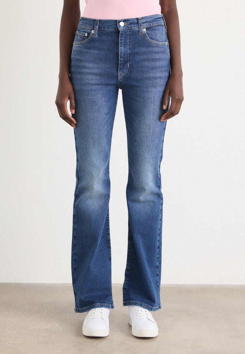 Bredde blå jeans laget av denim med middelsvask. Har frontlommer og knappefeste. Kombinert med hvite joggesko.