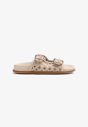 Sandalia beige con tiras de cuero trenzado, dos hebillas ajustables y suela plana con dibujo de color marrón claro.