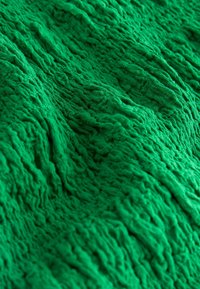 Tissu vert avec une texture froissée et chiffonnée créant un motif de surface tactile et irrégulier.