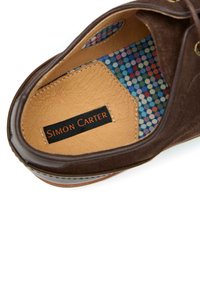 Brown suede shoe interior with hexagonal cutouts, featuring a multicolored dotted pattern lining. "Simon Carter" label visible.