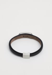 Orologio da polso con bracciale in pelle nera, chiusura rettangolare in argento e interno in brown texture, caratterizzato da un design minimalista e forma elegante.